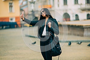 Young beautiful casual girl takes a selfie on her cell phone with sunglasses