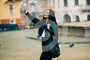 Young beautiful casual girl takes a selfie on her cell phone with sunglasses