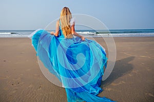Young beautiful caucasian blonde woman in long tull butterfly white blue dress on coast of sea.female running towards