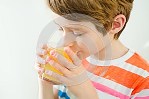 Young beautiful caucasian boy drinking orange juice from glass