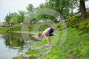 Young beautiful caucasian brunette girl doing yoga on a green lawn against the background of the river