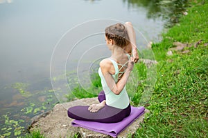 Young beautiful caucasian brunette girl doing yoga on a green lawn against the background of the river