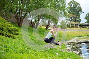 Young beautiful caucasian brunette girl doing yoga on a green lawn against the background of the river