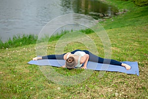 Young beautiful caucasian brunette girl doing yoga on a green lawn against the background of the river