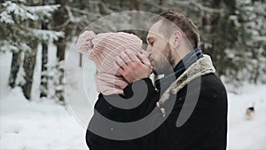 Young beautiful caucasian couple kissing under a snow in a winter forest. Couple having fun. Man pulls her hat over her