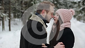 Young beautiful caucasian couple kissing under a snow in a winter forest. Couple having fun. Man pulls her hat over her