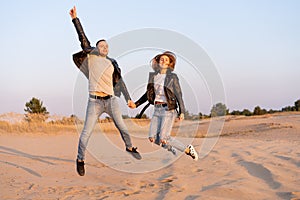 Young beautiful caucasian couple man and woman jumping holding hands on on sandy beach