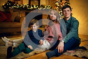 Young beautiful caucasian couple with their son posing on floor in a cozy Christmas interior