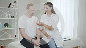 Young beautiful Caucasian doctor giving medical drops to mid-adult man in hospital ward. Portrait of professional