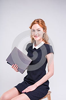 A young beautiful Caucasian female student sits on a chair in the studio on a white background. She is wearing a dress