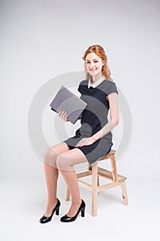 A young beautiful Caucasian female student sits on a chair in the studio on a white background. She is wearing a dress