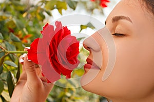 Young beautiful Caucasian girl smelling red roses in the garden on sunny day