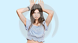 Young beautiful caucasian girl wearing casual clothes doing bunny ears gesture with hands palms looking cynical and skeptical