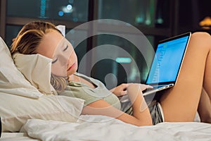 Young beautiful, caucasian, red haired, internet addicted woman working bored, sleepless and tired on her laptop in bed