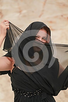 Young beautiful Caucasian woman in black chiffon dress posing in desert landscape with sand.