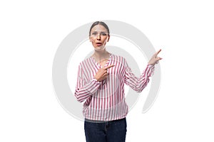 young beautiful caucasian woman with black hair gathered in a ponytail dressed in a striped blouse points her hand to