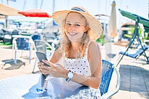 Young beautiful caucasian woman with blond hair smiling happy outdoors using smartphone sitting at bar terrace