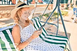 Young beautiful caucasian woman with blond hair smiling happy outdoors using smartphone