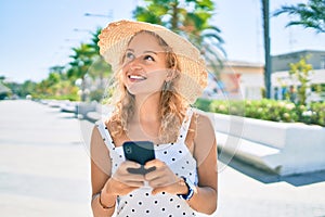 Young beautiful caucasian woman with blond hair smiling happy outdoors using smartphone