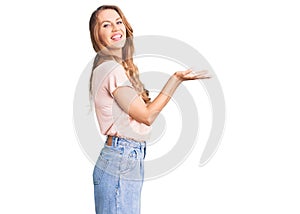 Young beautiful caucasian woman with blond hair wearing casual clothes pointing aside with hands open palms showing copy space,