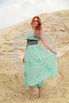 Young beautiful Caucasian woman in blue long shiffon dress posing in desert landscape with sand.