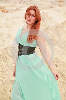 Young beautiful Caucasian woman in blue long shiffon dress posing in desert landscape with sand.