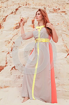 Young beautiful Caucasian woman in colorful long summer chiffon dress posing in desert landscape with sand.