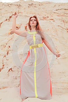 Young beautiful Caucasian woman in colorful long summer chiffon dress posing in desert landscape with sand.