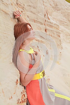 Young beautiful Caucasian woman in colorful long summer chiffon dress posing in desert landscape with sand.