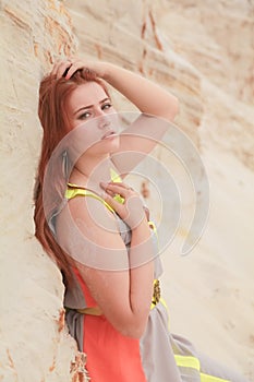 Young beautiful Caucasian woman in colorful long summer chiffon dress posing in desert landscape with sand.