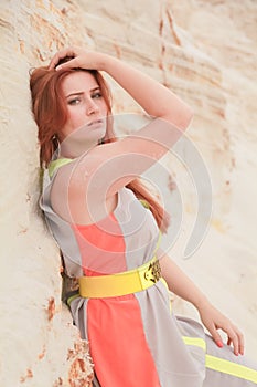 Young beautiful Caucasian woman in colorful long summer chiffon dress posing in desert landscape with sand.