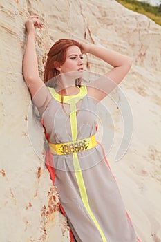 Young beautiful Caucasian woman in colorful long summer chiffon dress posing in desert landscape with sand.