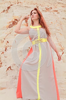 Young beautiful Caucasian woman in colorful long summer chiffon dress posing in desert landscape with sand.