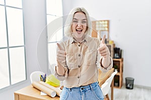 Young beautiful caucasian woman at construction office approving doing positive gesture with hand, thumbs up smiling and happy for