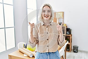 Young beautiful caucasian woman at construction office success sign doing positive gesture with hand, thumbs up smiling and happy