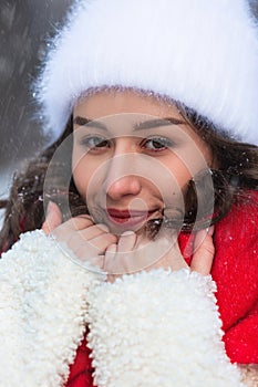 Young beautiful caucasian woman with dark hair wearing white hat and red scarf during snowfall on winter day.