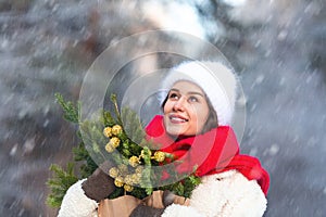 Young beautiful caucasian woman with dark hair wearing white hat and red scarf during snowfall on winter day.