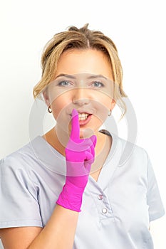 Young beautiful caucasian woman doctor, beautician doing silent gesture pressing his index finger to his lips isolated