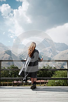 Young beautiful caucasian woman drinking wine at balcony at apartments in mountain