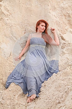 Young beautiful Caucasian woman in evening shiffon dress posing in desert landscape with sand.