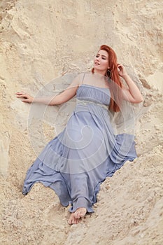 Young beautiful Caucasian woman in evening shiffon dress posing in desert landscape with sand.