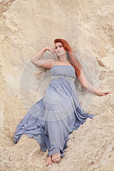 Young beautiful Caucasian woman in evening shiffon dress posing in desert landscape with sand.