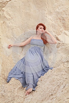 Young beautiful Caucasian woman in evening shiffon dress posing in desert landscape with sand.