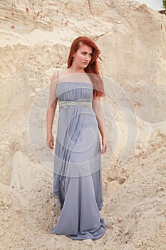 Young beautiful Caucasian woman in evening shiffon dress posing in desert landscape with sand.