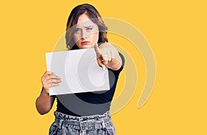 Young beautiful caucasian woman holding blank empty paper pointing with finger to the camera and to you, confident gesture looking