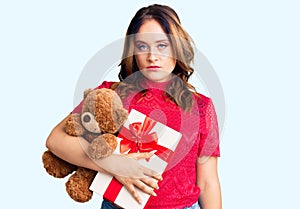 Young beautiful caucasian woman holding gift and teddy bear thinking attitude and sober expression looking self confident