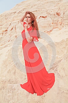 Young beautiful Caucasian woman in long bright outfit posing in desert landscape with sand.