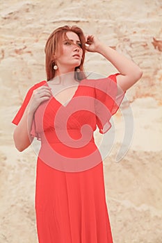 Young beautiful Caucasian woman in long bright outfit posing in desert landscape with sand.
