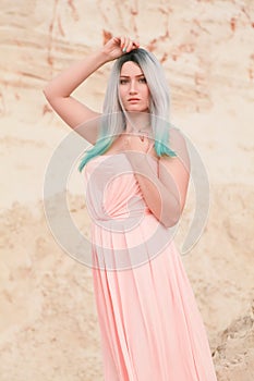 Young beautiful Caucasian woman in long pink dress posing in desert landscape with sand.