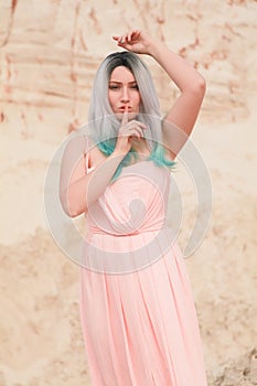 Young beautiful Caucasian woman in long pink dress posing in desert landscape with sand.